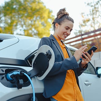 Woman leaning on her car while it charges.